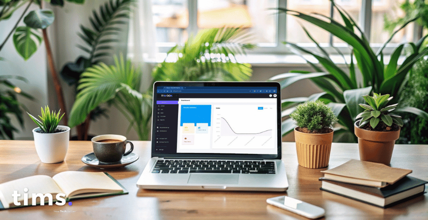 A laptop placed on a wooden desk displaying a dashboard interface of 'TIBOOK'. The dashboard features a sidebar menu on the left with options and a graphical sales report on the right. The screen shows various statistics and charts. The workspace includes a coffee cup, a small potted plant, a notebook, and a smartphone, creating a professional and cozy setting.
                    